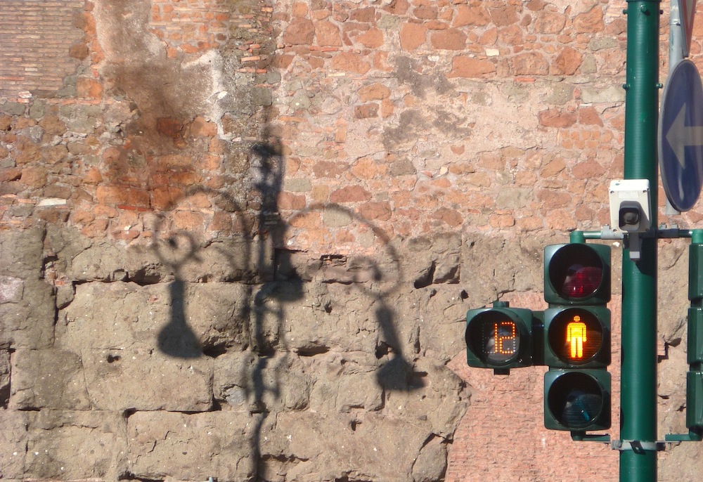 Ombre d'un lampadaire ouvragé sur un mur de briques et feu tricolore