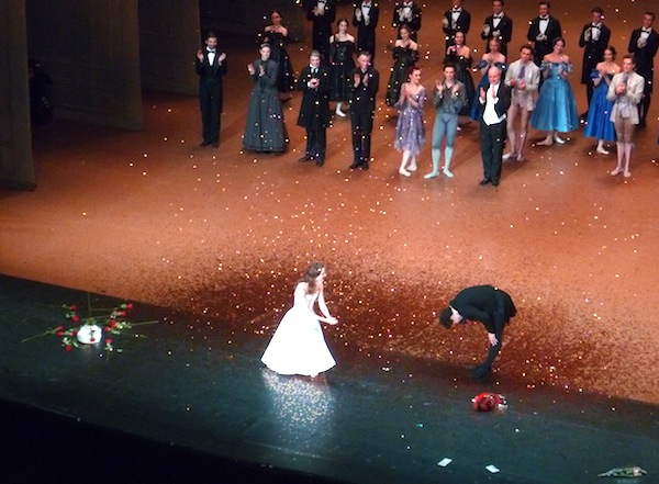 Corps de ballet et solistes derrière le couple principal et bouquets de fleurs sur le devant de la scène