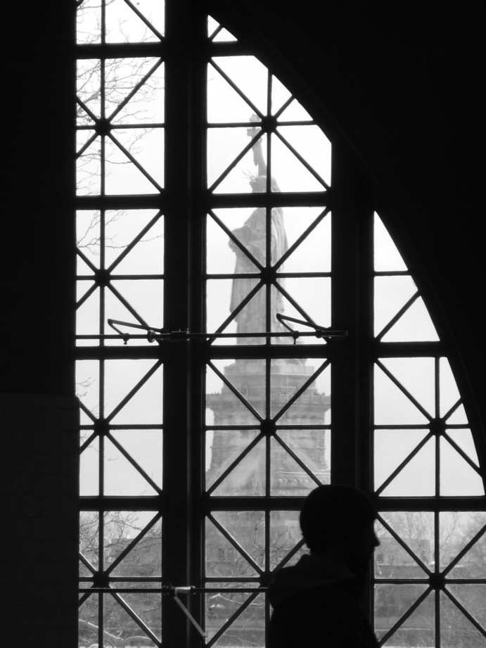 Statue de la Liberté visible derrière une fenêtre d'Ellis Island et silhouette en sens inverse à contre-jour