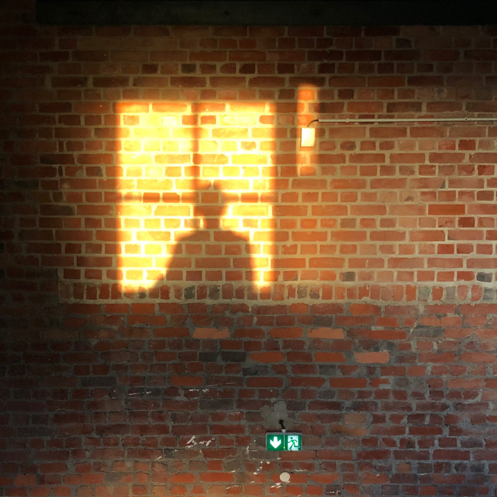 Sur un mur de briques intérieur, découpe dorée par le soleil d'hiver d'une fenêtre avec une silhouette