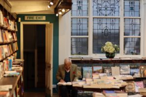 Photo floue où un monsieur bien habillé avec une pochette lit dans une magnifique librairie avec un vitrail