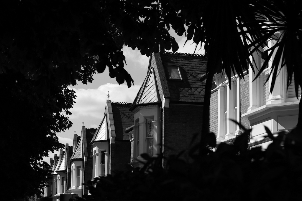 Rangée de maisons avec bow windows, encadrée par des feuillages sombres