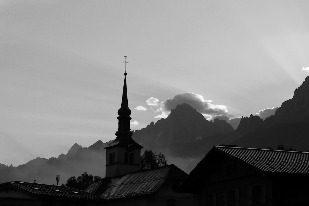 Rayons de lumières qui percent derrière les montagnes, avec la silhouette d'un clocher au premier plan