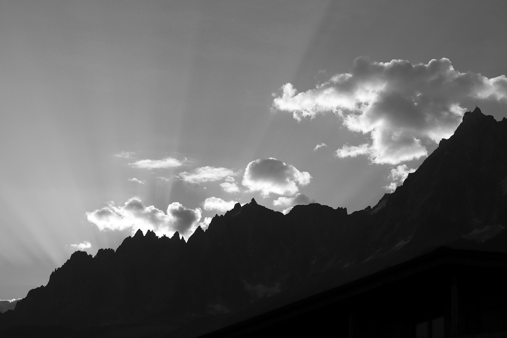 Rayons du soleil levant qui illuminent les nuages derrière une chaîne de montagnes à contrejour.