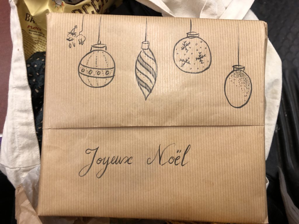 paquet cadeau kraft avec des boules de Noël dessinées dessus… et une souris avec un bonnet de Noël, suspendues comme les boules par la queue