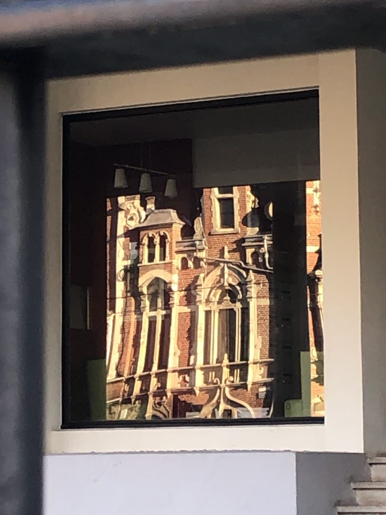 Dans une vitre carrée, reflet de l'immeuble ouvragé en brique et moulures d'en face