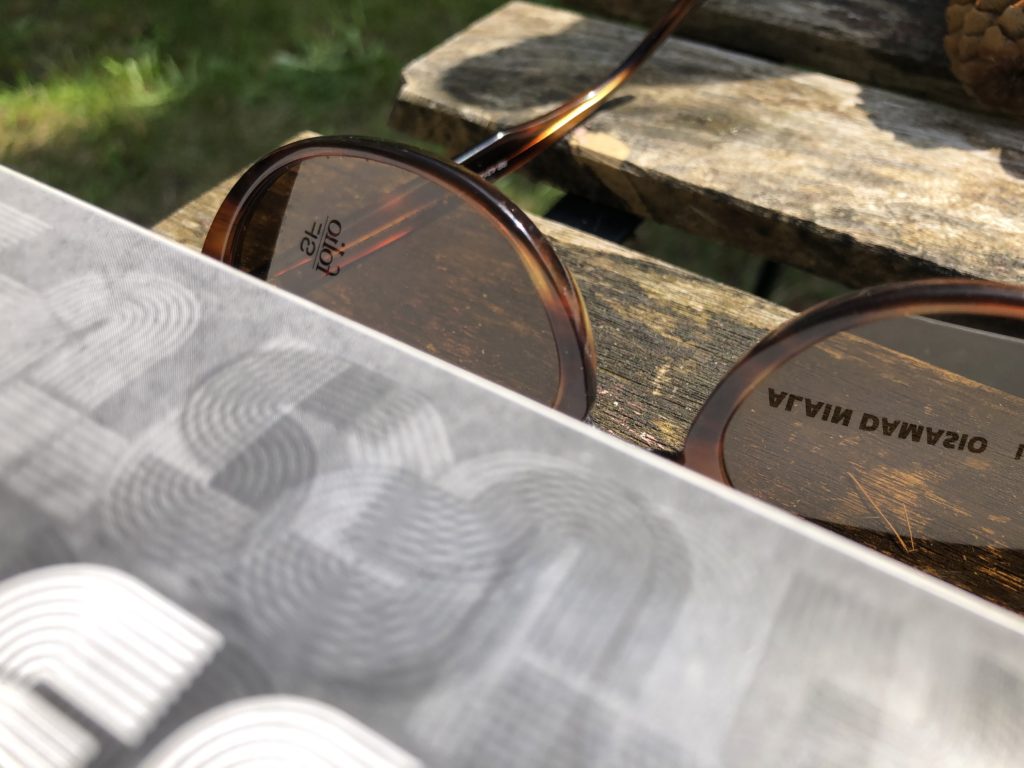 Gros plan d'une couverte et reflets dans des lunettes de soleil : "Folio SF" et "Alain Damasio" écrit à l'envers