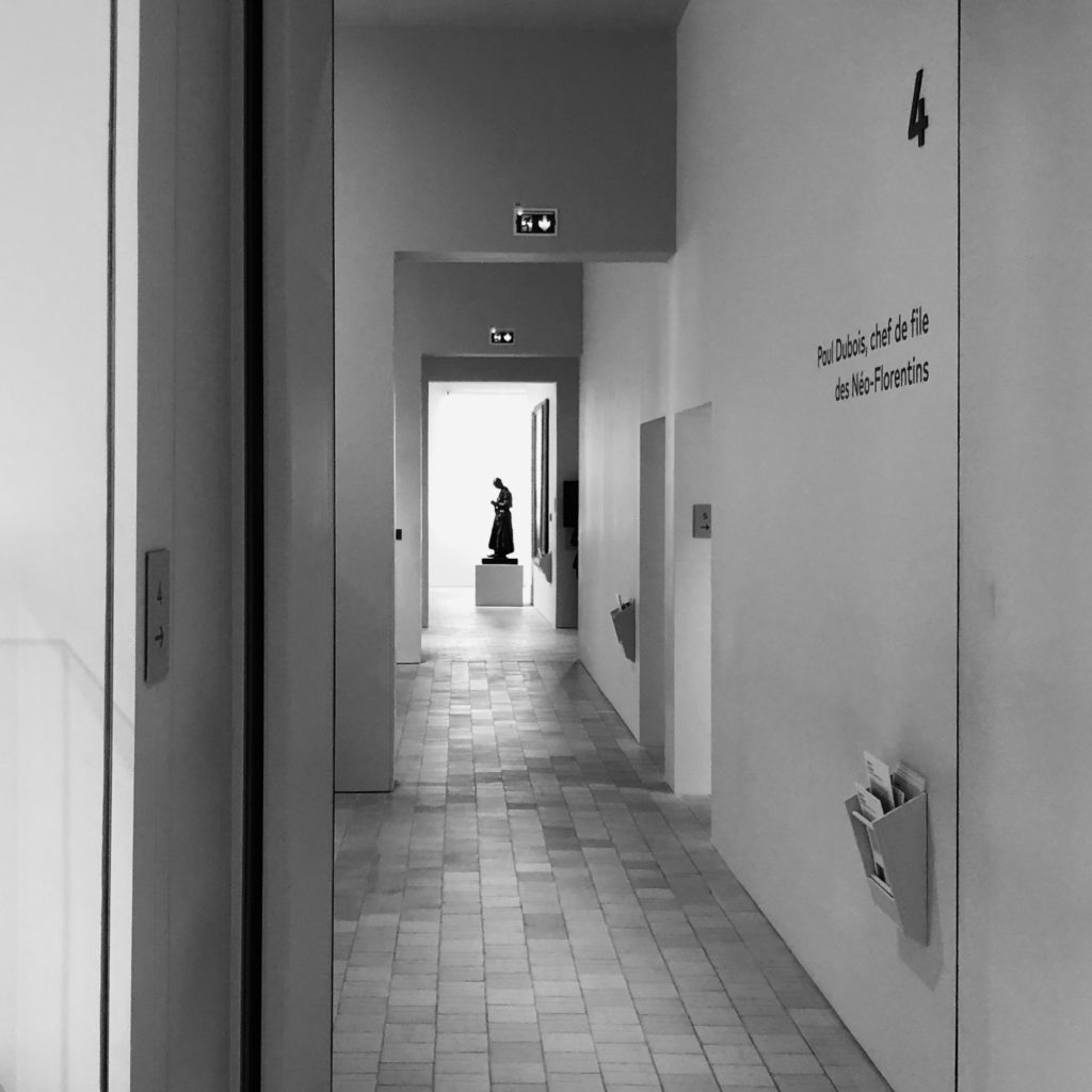 Couloir vide du musée, avec la silhouette d'une statue en bronze tout au bout
