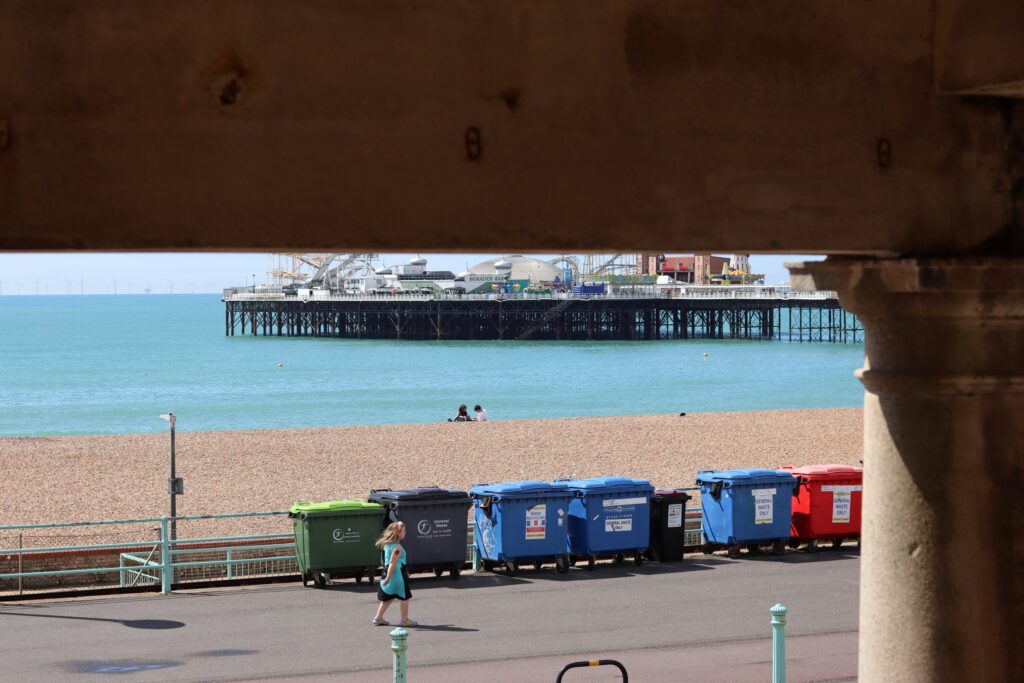 Plage de Brighton au second plan, derrière un fronton sombre et une rangée de poubelles