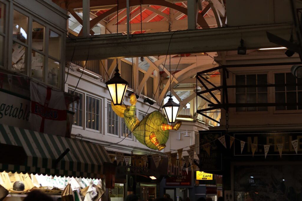 Alice (au pays des merveilles) illuminée et figée dans sa chute, accrochée au plafond de la halle