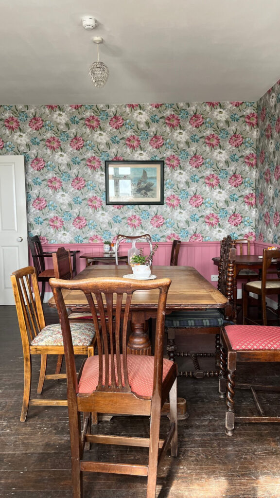 Photo du salon de thé avec les chaises dépareillées et toujours le papier peint à fleurs