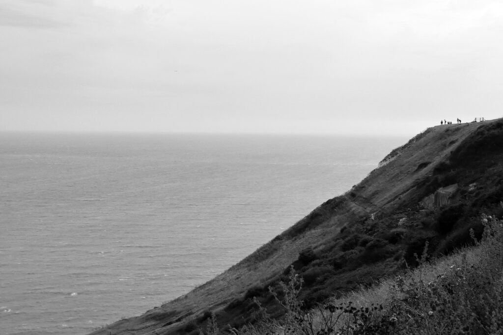 Dénivelé de la falaise et minuscules silhouettes humaines en haut, face à la mer