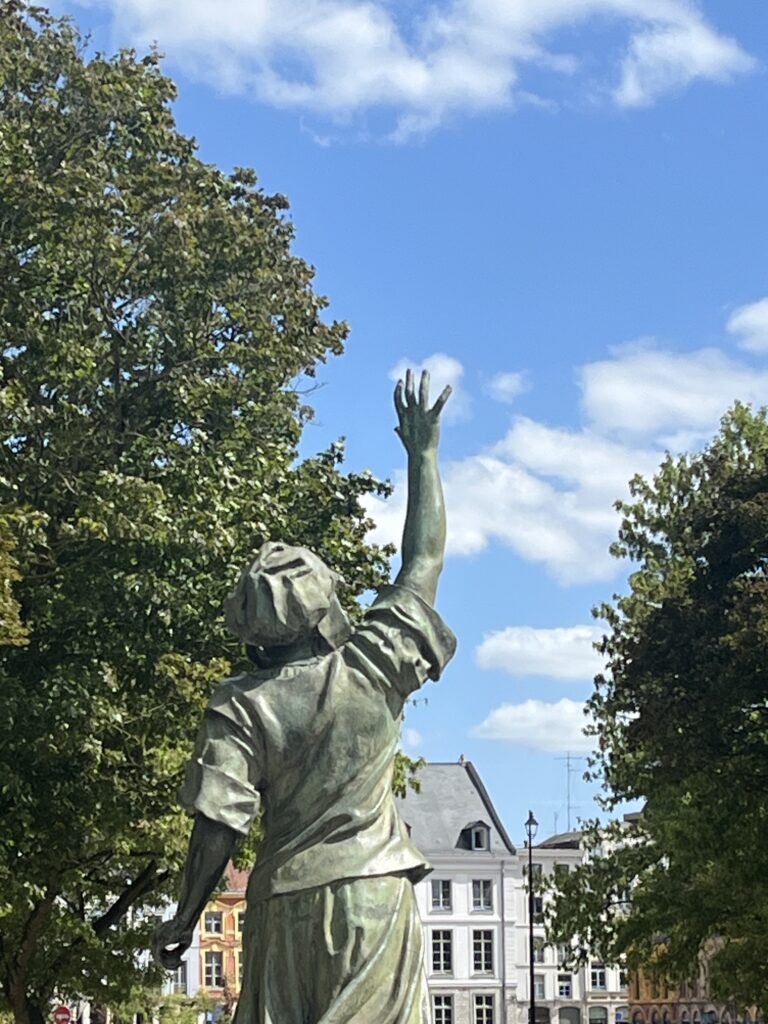 Statue vue de dos, main levée, un petit nuage comme une boule de coton au niveau de sa main